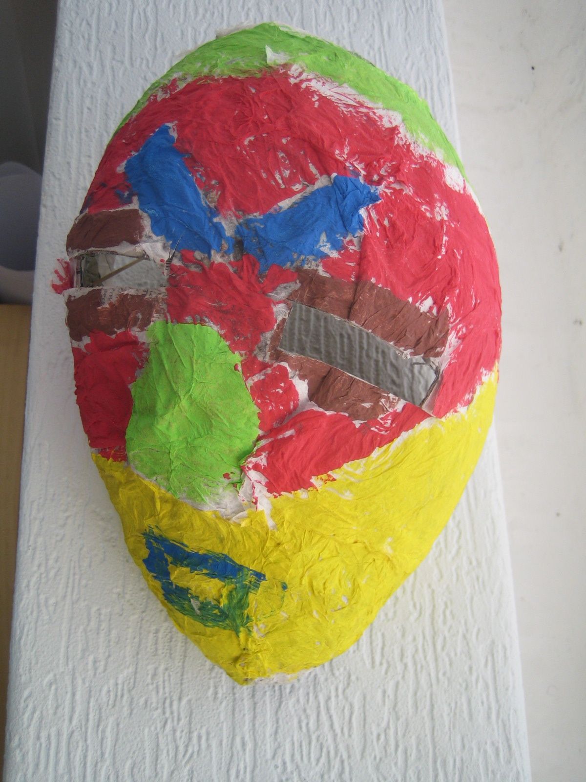 a colorful painted face on a white surface - Masker Maken Van Papier Mache